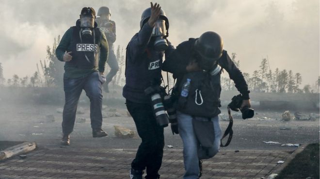 Фотожурналисты и видеожурналисты в противогазах бегут от слезоточивого газа во время столкновений с израильскими силами возле израильского контрольно-пропускного пункта в городе Рамаллах на Западном берегу.