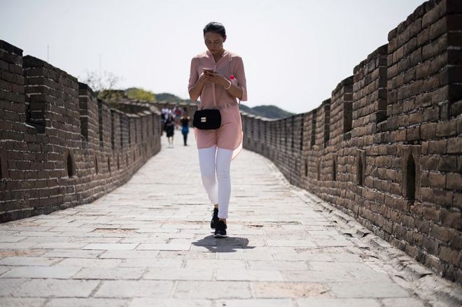 Китайская женщина гуляет, когда она печатает на своем смартфоне на Великой стене в Мутианью, недалеко от Пекина, 23 апреля 2016 года.