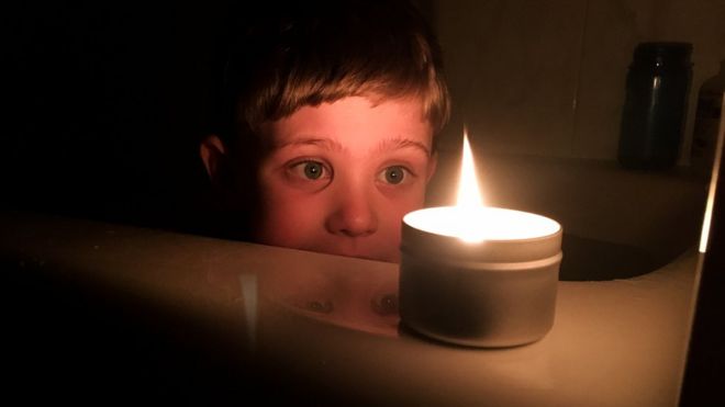 Ребенок смотрит на свечу в темной комнате (фото из архива)