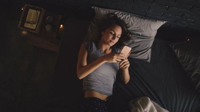 Mulher usa celular na cama