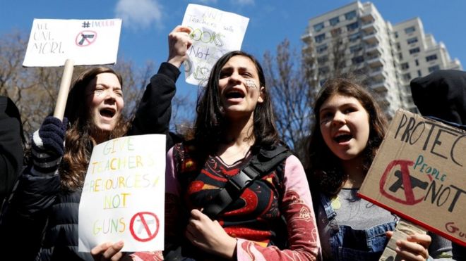 Трое учеников держат различные знаки в школьной забастовке в Нью-Йорке