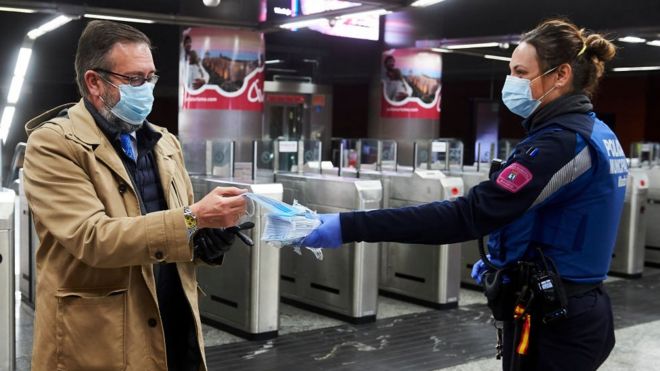 Miembro de la policía entrega mascarillas a un viajero del metro de Madrid.