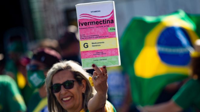 A woman in Brazil at a pro-Bolsonaro rally holds a sign designed to look like a box of ivermectin