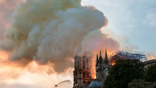 Пожарный использует шланг для тушения пламени, вздымающегося с крыши собора Нотр-Дам