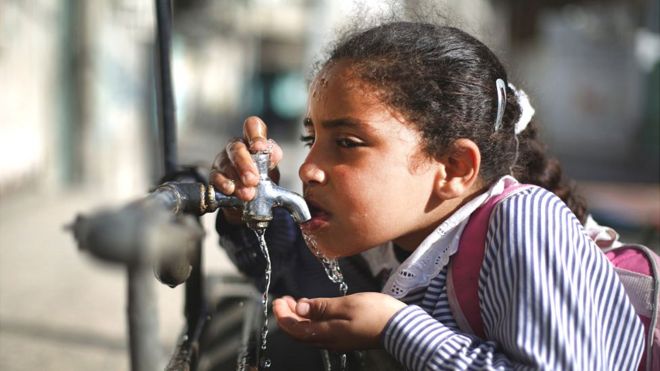 Niña tomando agua de una canilla en Gaza