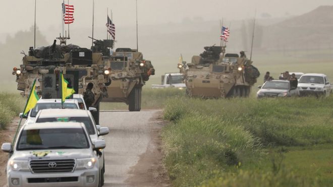 Курдские боевики из Народного подразделения защиты (YPG) проезжают перед американской военной бронетехникой в ??северной Сирии (28 апреля 2017 г.)