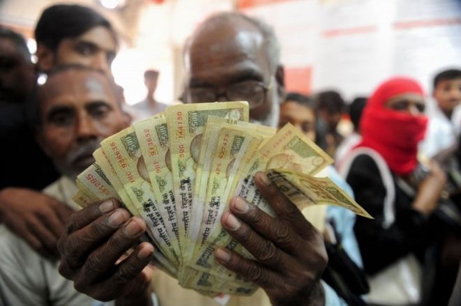Индийский мужчина держит старые версии банкноты номиналом в 500 рупий, когда люди стоят в очереди внутри банка, чтобы внести 500 и 1000 банкнот в индийской рупии в деревне Рахимапур на окраине Аллахабада 10 ноября 2016 года