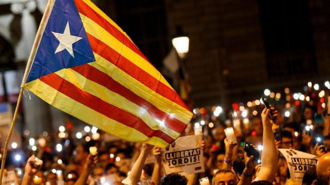 People hold candles and a Catalan pro-independence "Estelada" flag during a demonstration in Barcelona against the arrest of two Catalan separatist leaders on October 17, 2017.