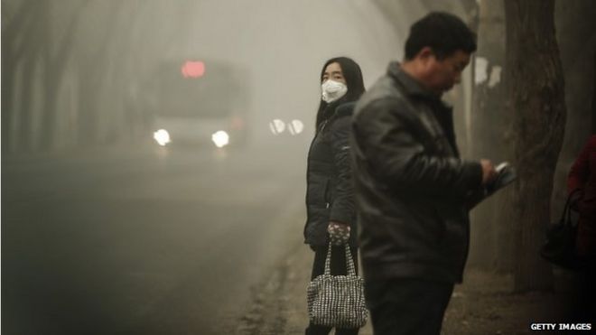 A woman wears a face mask next to traffic shrouded in heavy smog on December 1, 2015 in Beijing