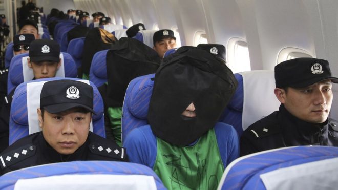 На этом фото, опубликованном агентством Синьхуа, китайские подозреваемые, причастные к мошенничеству с проволокой, в центре сидят в самолете, когда они прибывают в международный аэропорт Пекин Столичный в Пекине в среду, 13 апреля 2016 года