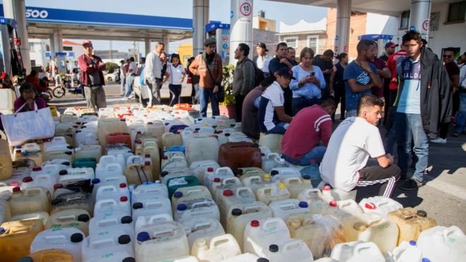 Personas sentadas frente a una gasolinera.