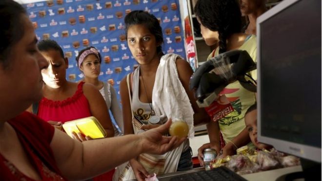 Люди платят кассиру за свои товары в кассе супермаркета в Каракасе 20 октября 2015 года.