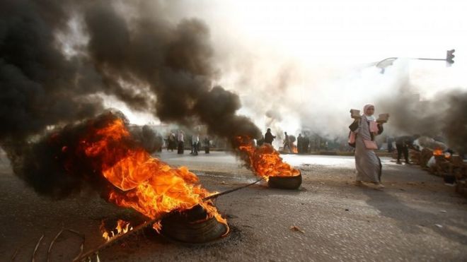 Митингующие с брусчаткой проходят мимо горящих шин в Хартуме, Судан. Фото: 3 июня 2019 года