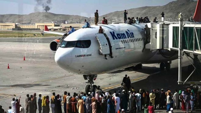 People clamber on top of planes as smoke rises in the distance