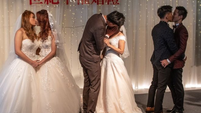 Three couples kiss during wedding ceremony