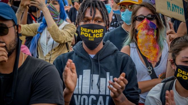 Manifestante usando una mascarilla que dice "Defund the Police".