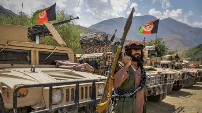 An Afghan soldier holds a rocket propelled grenade and stands in front of military vehicles