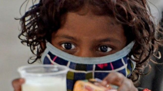 A poor child takes a glass of milk and a packet of biscuits during a free glass of milk and biscuit packet distribution organised by Kolkata police amid coronavirus emergency in Kolkata, India, 23 May, 2021. In