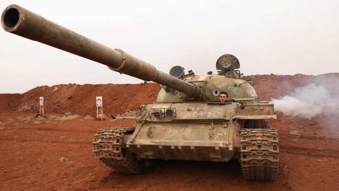 Сирийский мятежный истребитель ведет танк, который был выведен из демилитаризованной зоны вдоль линии фронта в провинции Идлиб (9 октября 2018 года)