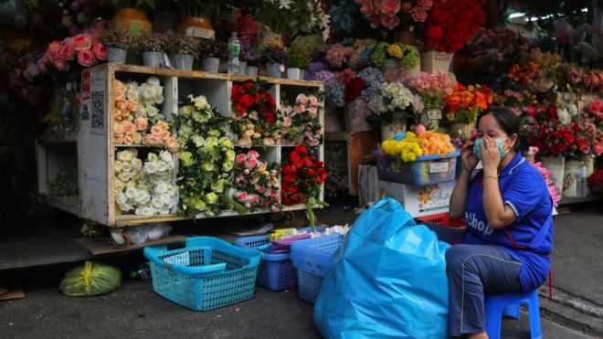 Женщина в маске работает на цветочном киоске в Бангкоке, Таиланд