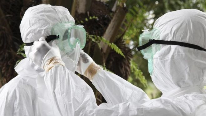 Либерийские медсестры надевают защитную одежду в качестве подготовки для ношения тела жертвы Эболы для захоронения (8 августа 2014 года)