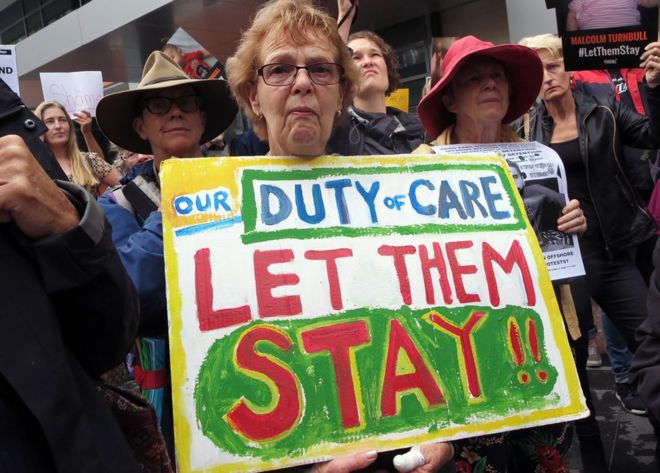 Женщина, протестующая против политики задержания в Австралии, держит плакат с надписью: «Наш долг заботы: пусть они останутся».
