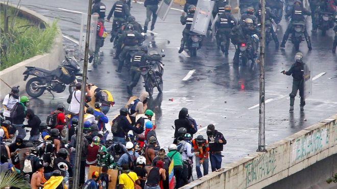 Сотрудник сил безопасности ОМОНа указывает, что, по-видимому, пистолет на толпу демонстрантов во время митинга против правительства президента Венесуэлы Николаса Мадуро в Каракасе, 19 июня