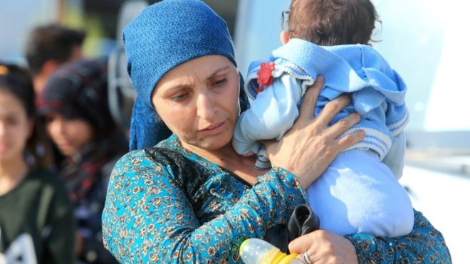 A displaced Syrian woman, who fled violence after the Turkish offensive in Syria, carries her baby