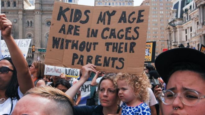 Протестующие с маленьким ребенком в руках с табличкой «Дети моего возраста находятся в клетках без родителей»