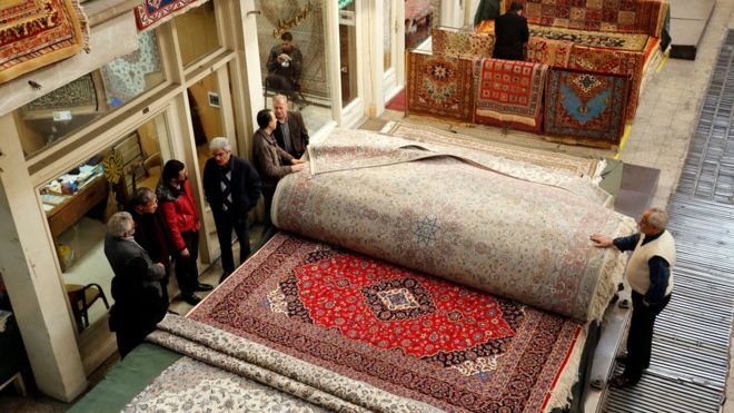 Покупатели и продавцы ковров стоят рядом с коврами на Большом базаре Тегерана в Иране.