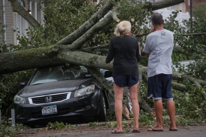 Люди смотрят на упавшее дерево на машине после тропического шторма Исайас в районе Рокавей в Квинсе, Нью-Йорк, США, 4 августа 2020 г.