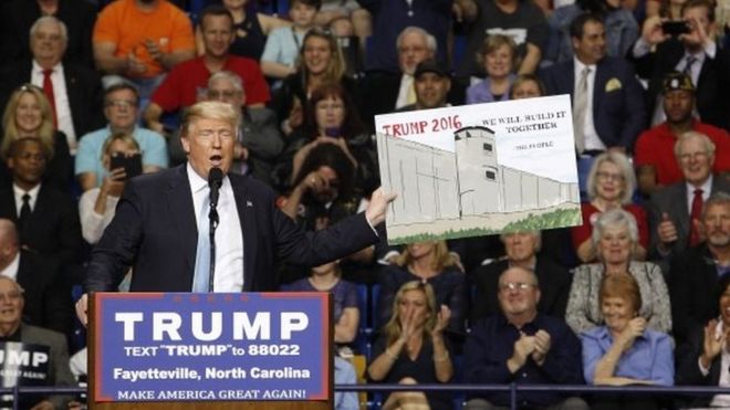 Кандидат в президенты США от республиканцев Дональд Трамп держит знак в поддержку своего плана строительства стены между Соединенными Штатами и Мексикой, которую он позаимствовал у аудитории на своем предвыборном митинге в Фейетвилле, штат Северная Каролина, 9 марта 2016 года