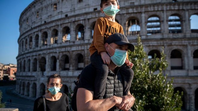 : Туристы в масках посещают район Колизея 24 февраля 2020 года в Риме, Италия. Итальянское правительство объявило чрезвычайное положение 31 января, и сегодня коронавирус (Covid-19) унес шестую жертву в Италии, 80-летний мужчина из Кастильоне-д'Адда, скончавшийся в миланской больнице Сакко