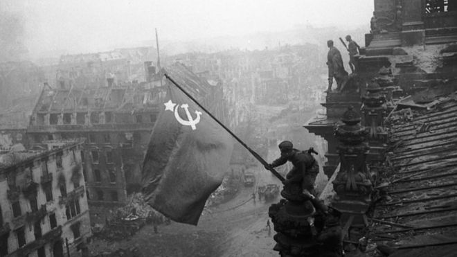 A Soviet soldier pictured hoisting a flag over the Reichstag in 1945