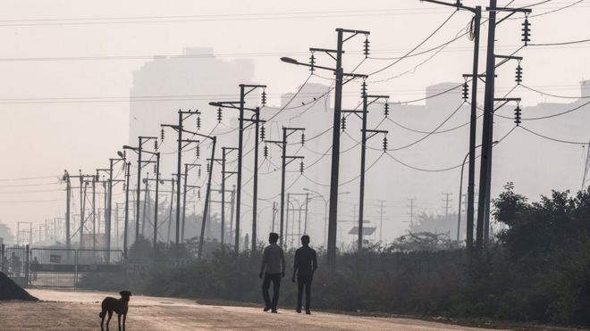 Два индийских мужчины проходят мимо проводов электричества около недавно построенных жилых башен в Ноиде, городе-спутнике Нью-Дели.