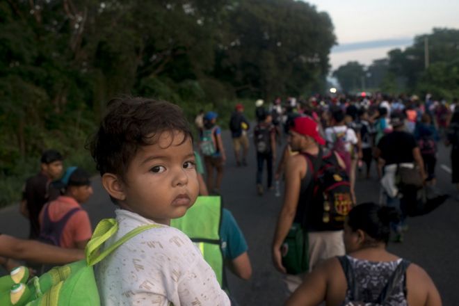 Отец несет своего ребенка на своих плечах, когда он идет по дороге к мексиканскому городу Тапачула