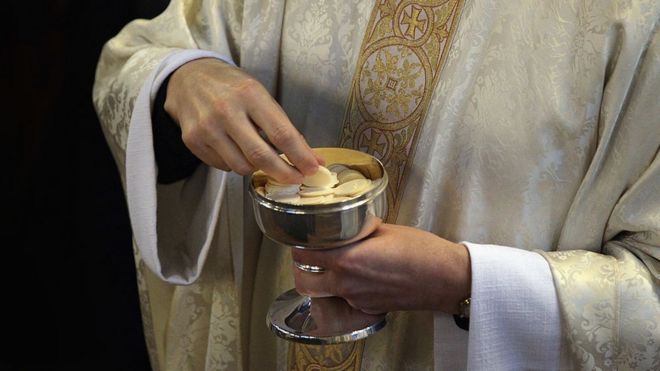 Священник держит вафли для причастия
