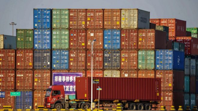 Грузовик перевозит контейнер рядом со штабелированными контейнерами в порту Циндао в китайской провинции Шаньдун 12 октября 2018 года.