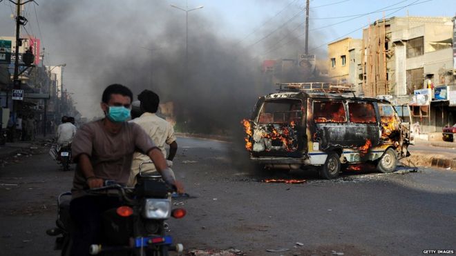 Пакистанцы проезжают мимо горящей машины в Карачи после ареста Альтафа Хуссейна в Лондоне.