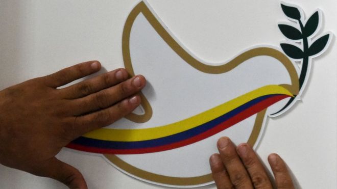 Un hombre intenta ajustar sobre una pared una cartulina con una paloma de la paz y la bandera de Colombia.