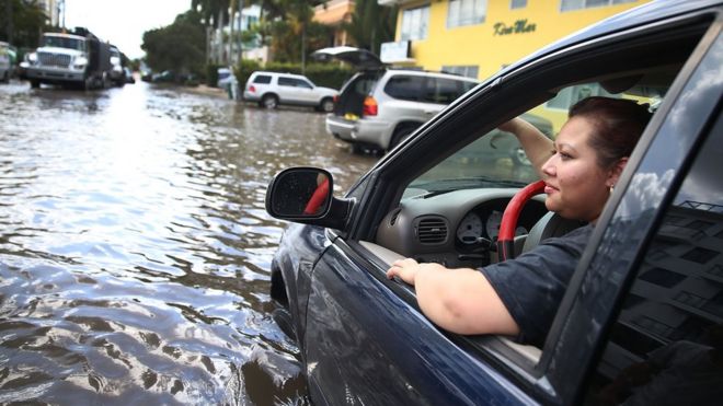 Сэнди Гарсия сидит в своем автомобиле, который застрял на затопленной улице, вызванной сочетанием лунной орбиты, вызвавшей сезонные приливы, и, как многие считают, повышением уровня моря из-за изменения климата 30 сентября 2015 года в Форт-Лодердейле, Флорида | || Видно, что дом окружен паводковыми водами, вызванными сочетанием лунной орбиты, вызвавшей сезонные приливы, и то, что многие считают повышением уровня моря из-за изменения климата в Форт-Лодердейле, Флорида