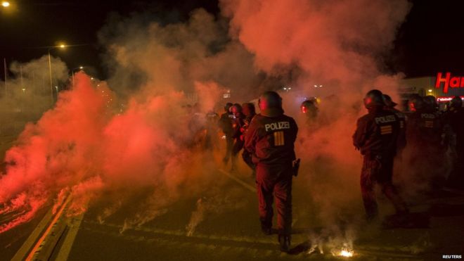 Полиция проходит между вспышками, брошенными правыми демонстрантами, которые выступают против доставки просителей убежища в жилой комплекс в Хайденау, Германия (22 августа 2015 г.)
