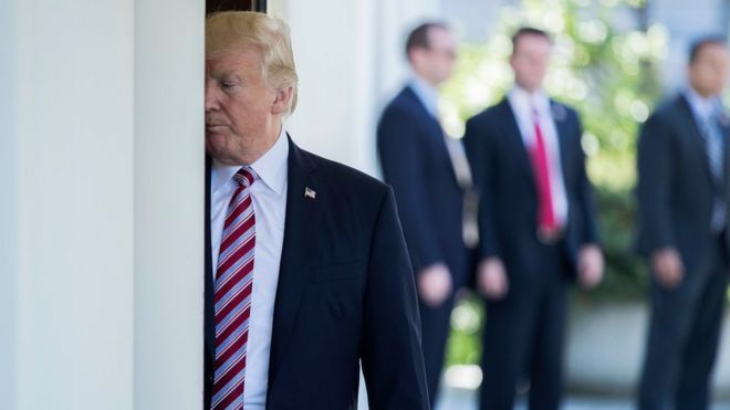 Donald Trump stands half hidden behind a post at the White House
