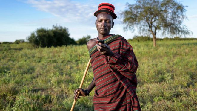 Угандийский фермер смотрит на телефон в поле
