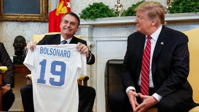 Ao lado de Donald Trump, Jair Bolsonaro segura camisa da seleção dos EUA com o nome dele