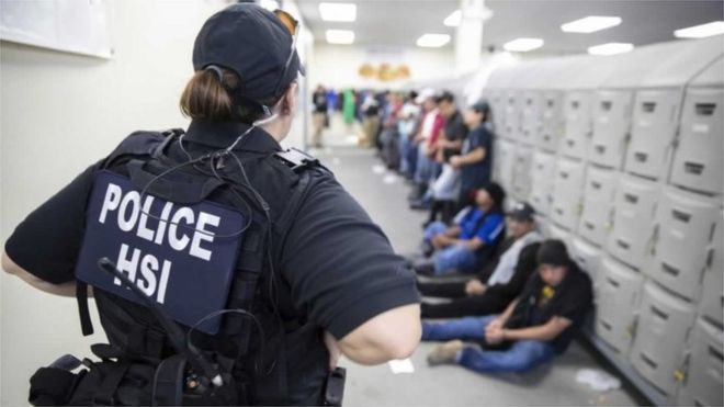 На этом изображении, опубликованном Управлением иммиграционной и таможенной службы США (ICE), показан офицер отдела расследований внутренней безопасности (HSI), охраняющий подозреваемых в незаконном перемещении иностранцев 7 августа 2019 г.