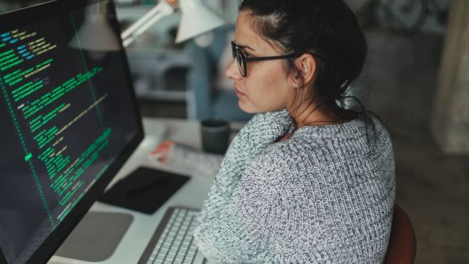 Mujer frente a una computadora manejando lenguaje de código para web.
