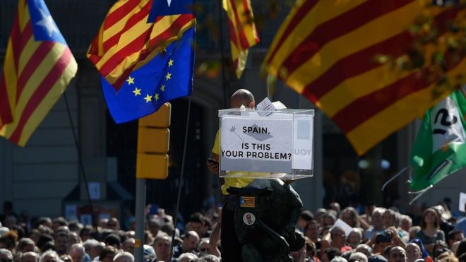 Люди на большой демонстрации в Барселоне, держат каталонские флаги и символическую урну для голосования