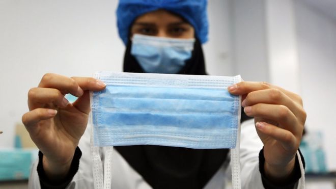 A women holds up a medical mask in a factory now open 24 hours a day in Tehran, Iran