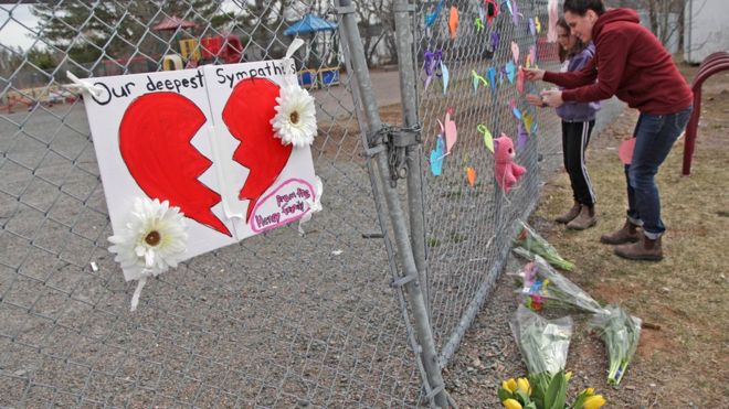 : Женщина и ее дочь кладут сердце на забор у растущего мемориала перед школой Деберта 20 апреля 2020 г.